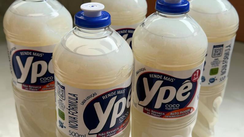 Seis garrafas plásticas transparentes contendo detergente líquido branco da marca Ypê, variante coco, com tampas azuis. Rótulos exibem informações de produto e validade.