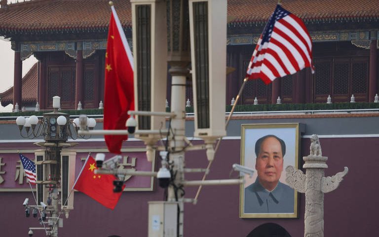 Bandeiras da China e dos Estados Unidos estão hasteadas em postes na Praça Tiananmen, Pequim, com o retrato de Mao Tsé-Tung visível ao fundo na parede do portão da Cidade Proibida.