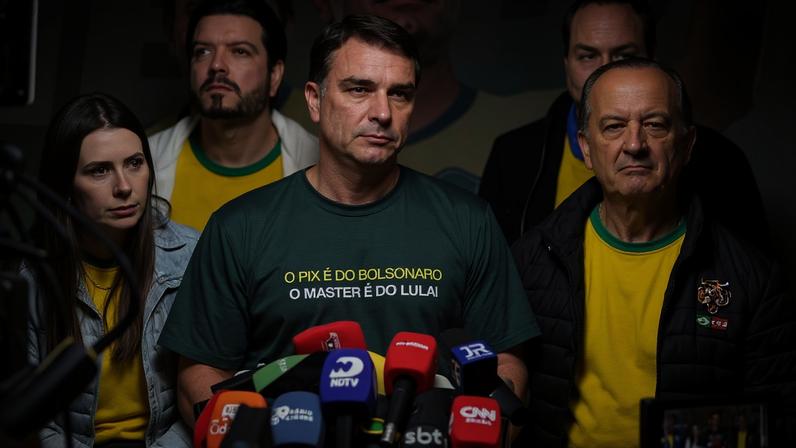 Cinco pessoas em coletiva de imprensa, três vestem amarelo e verde, uma usa camiseta verde com frase O Pix é de Bolsonaro O Master é do Lula. Microfones de várias emissoras estão à frente.
