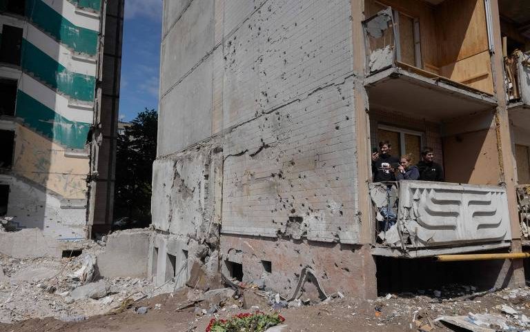 Moradores locais observam a vista na varanda de um prédio residencial danificado após ataques de drones e mísseis russos em Kiev