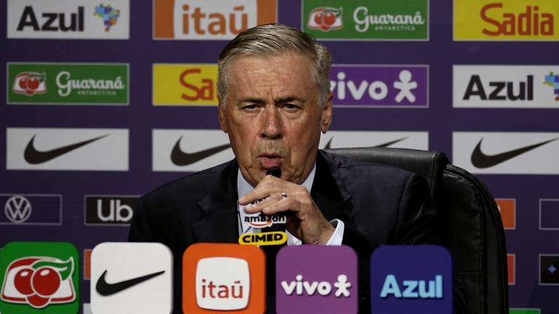 Homem de cabelos grisalhos veste terno escuro e fala em microfone durante coletiva. Painel ao fundo exibe logotipos de patrocinadores como Azul, Itaú, Guaraná Antarctica, Sadia, Nike e Vivo.