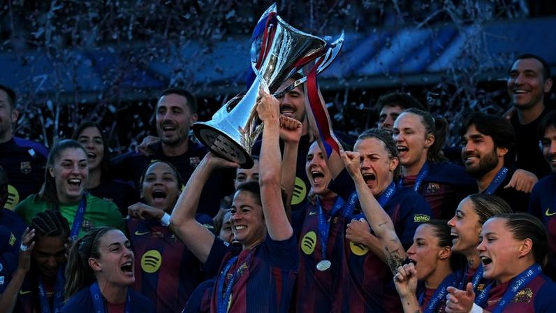 Jogadoras do Barcelona vestindo uniformes azul e grená celebram levantando troféu em estádio, com confetes dourados caindo ao redor.