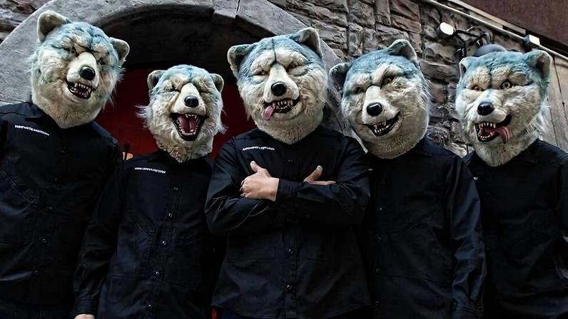 Cinco pessoas vestem camisas pretas e máscaras realistas de lobo, posando alinhadas em frente a uma parede de pedra com arco. O cenário é externo, com iluminação natural e detalhes arquitetônicos visíveis ao fundo.