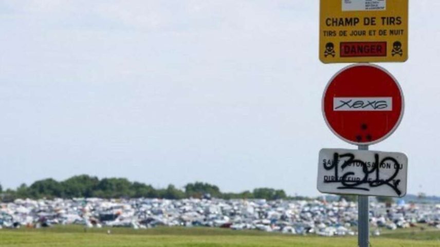 Vista geral mostra uma placa indicando ‘Campo de tiro, disparos dia e noite, perigo’ no local de um teknival, mega‑rave de música eletrônica geralmente ilegal na França, realizado em uma área militar em Cornusse, perto de Bourges, no centro da França, em 2 de maio de 2026.