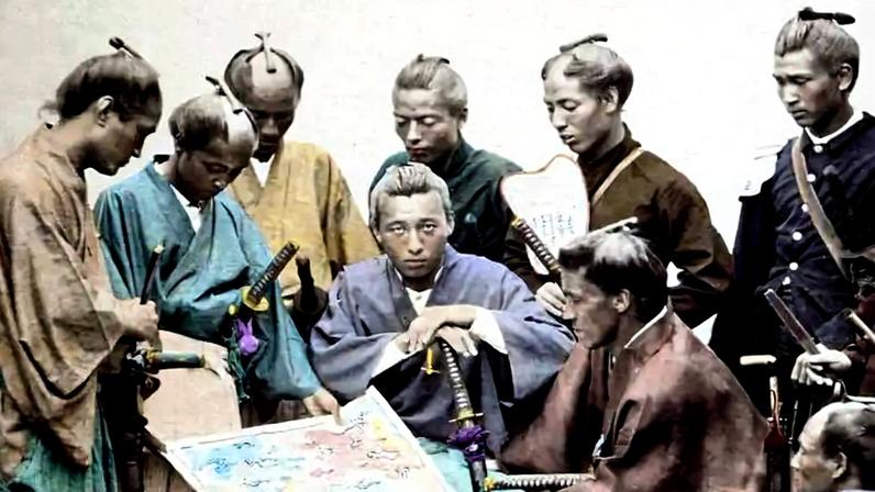 Oito homens vestidos com quimonos tradicionais e roupas militares japonesas do período samurai estão reunidos em um ambiente interno, observando atentamente um mapa colorido sobre uma mesa. Alguns seguram espadas e um deles segura um leque, indicando uma reunião estratégica.