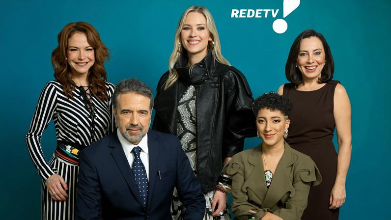Cinco apresentadores da RedeTV! posam juntos sobre fundo azul. Homem de terno azul escuro está sentado à frente. Atrás, quatro mulheres: uma com vestido listrado preto e branco, outra com casaco preto e vestido estampado, uma terceira com vestido marrom e a última com macacão verde-oliva.