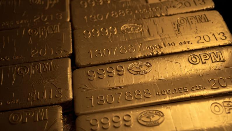 Várias barras de ouro empilhadas, cada uma com inscrições que indicam pureza 9999, números de série e o ano 2013. As barras têm acabamento brilhante e refletem luz dourada.
