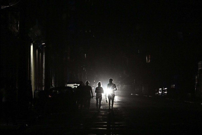 Pessoas caminham durante um apagão nacional em Havana, em 21 de março de 2026. - (crédito: YAMIL LAGE / AFP)