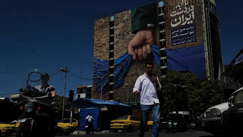 Moradores de Teerã passam por mural em fachada de prédio com a legenda em farsi "Sempre nas mãos do Irã", em alusão ao Estreito de Ormuz