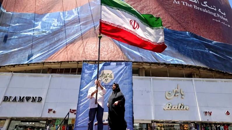 Iraniano agita a bandeira da República Islâmica em praça de Teerã, diante de outdoor que ironiza o presidente norte-americano - (crédito: Atta Kenare/AFP)