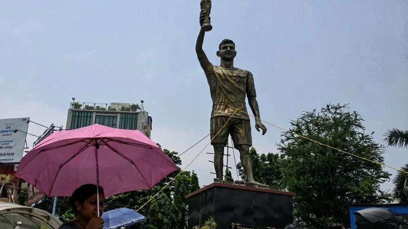 Passageiros passam por uma estátua do jogador de futebol argentino Lionel Messi, que foi amarrada com cordas para maior estabilidade e proteção contra chuva e tempestades, antes de ser reinstalada em um local mais seguro, em Calcutá, em 27 de maio de 2026 - (crédito: DIBYANGSHU SARKAR / AFP)