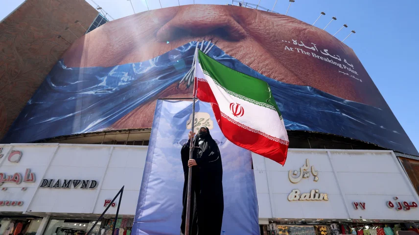 A woman holds the Iranian flag in front of an anti-US billboard referring to President Donald Trump and the Strait of Hormuz, at the Valiasr Square in Tehran on May 10.