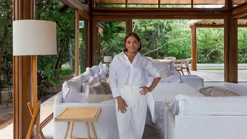 RETRATO | Heloísa Périssé na sala de estar, com sofá, poltrona e pufe, todos em sarja branca, da Velha Bahia. Produção da loja Bizâncio. Vigas e pilares de eucalipto. Obra civil executada pela ENG Construções