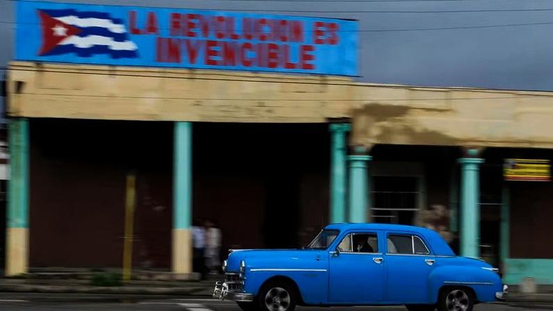 Um carro Dodge ano 1949 usado como táxi passa sob uma faixa com os dizeres 'A revolução é invencível' em Havana, Cuba — Foto: Reuters