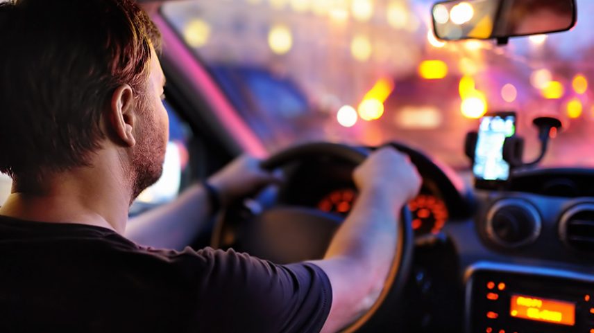 Motorista masculino dirige um carro durante o engarrafamento da noite. Vista interior.