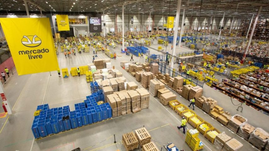 Grande centro de distribuição do Mercado Livre com trabalhadores movimentando caixas e produtos em diversas áreas de logística.