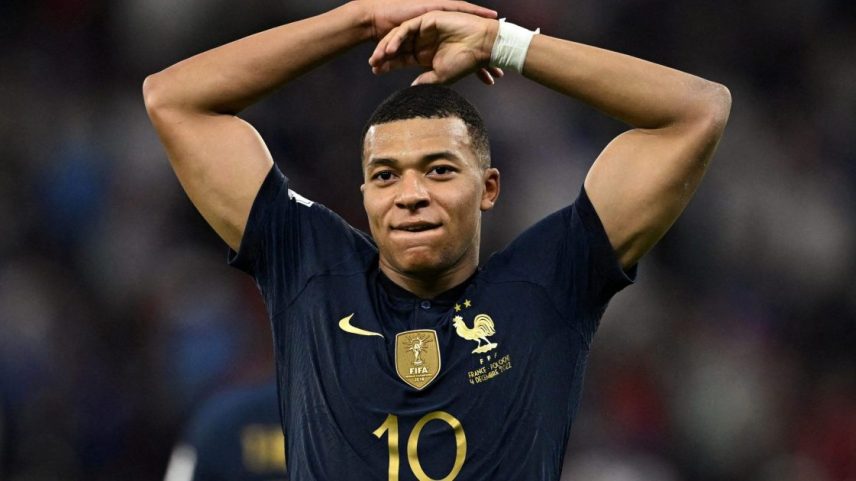 Kylian Mbappé, jogador da França, camisa 10, com as mãos acima da cabeça e expressão séria em jogo de futebol.