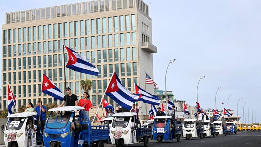 Cubanos em veículos elétricos carregam bandeiras do país enquanto passam pela Embaixada dos EUA durante manifestação em Havana