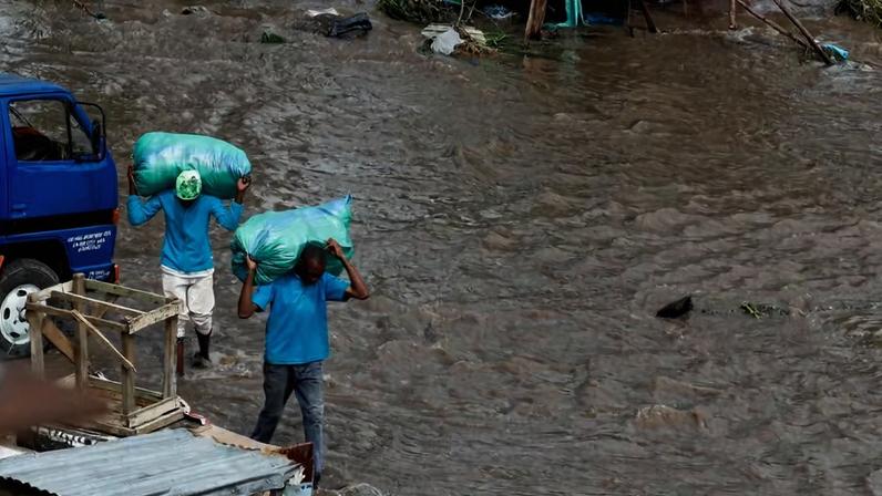 Pessoas carregam sacos enquanto caminham pela água da enchente após fortes chuvas na área de Ruai, em Nairóbi , Quênia, em 28 de abril de 2026