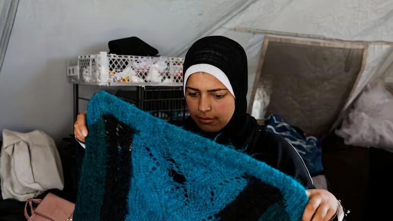 Amani Abu Selmi mostra peças de roupa comidas por ratos, em campo de refugiados palestinos em Gaza — Foto: Haseeb Alwazeer/Reuters