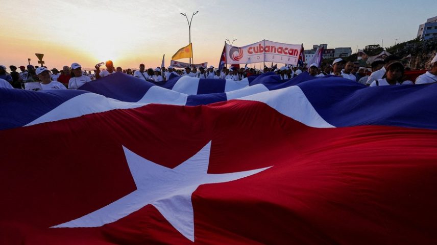 Pessoas marcham carregando uma bandeira nacional gigante de Cuba durante uma manifestação do Dia do Trabalho em Havana, Cuba