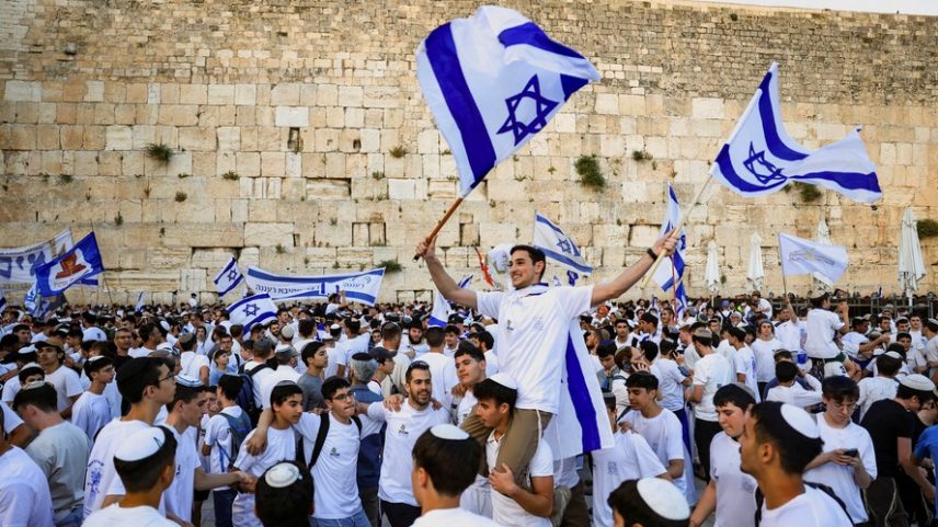 Pessoas acenam com bandeiras israelenses enquanto se reúnem na Praça do Muro das Lamentações, o local de oração mais sagrado do judaísmo, durante o Dia de Jerusalém, na Cidade Velha de Jerusalém, em 14 de maio de 2026