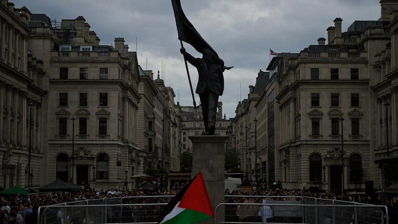 Pessoas seguram bandeiras palestinas ao lado de uma estátua, representando uma figura carregando uma bandeira cobrindo o rosto e descendo de um pedestal, do artista de rua britânico Banksy, durante uma marcha, realizada pela Palestine Solidarity Campaign, para marcar o 78º aniversário da Nakba e contra o comício "