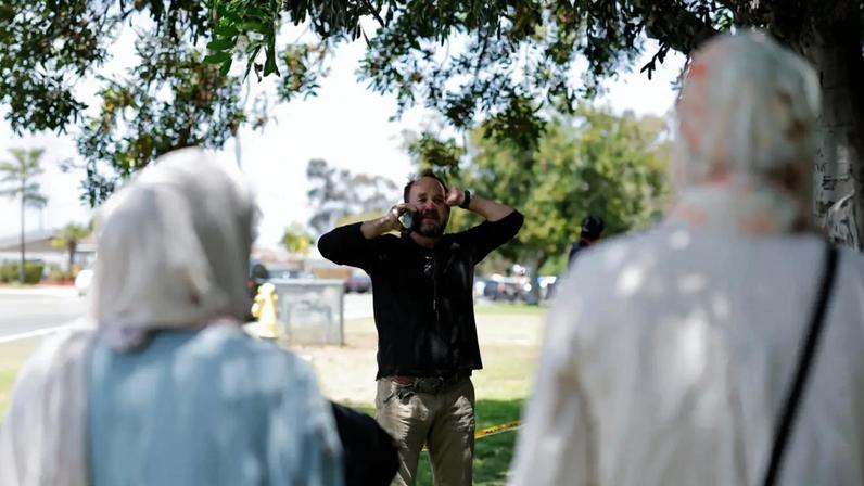 Um homem muçulmano usa o celular enquanto permanece com membros de sua comunidade na cena de um suposto ataque a tiros no Centro Islâmico, com fitas amarelas isolando a área, em San Diego, Califórnia, EUA, em 18 de maio de 2026. REUTERS/Mike Blake