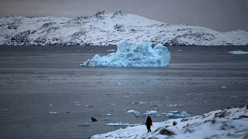 Uma pessoa caminha na costa enquanto um pequeno iceberg flutua no mar perto de Nuuk, Groenlândia — Foto: REUTERS/Stoyan Nenov