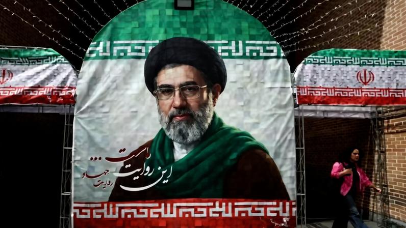 Uma mulher caminha ao lado de uma faixa com a foto do novo Líder Supremo do Irã, Mojtaba Khamenei, em Teerã, Irã, 8 de maio de 2026 — Foto: Majid Asgaripour/WANA (West Asia News Agency) via REUTERS