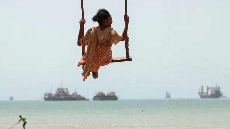 Criança brincando na praia em Bandar Abbas, Irã, com navios no Estreito de Ormuz ao longe
