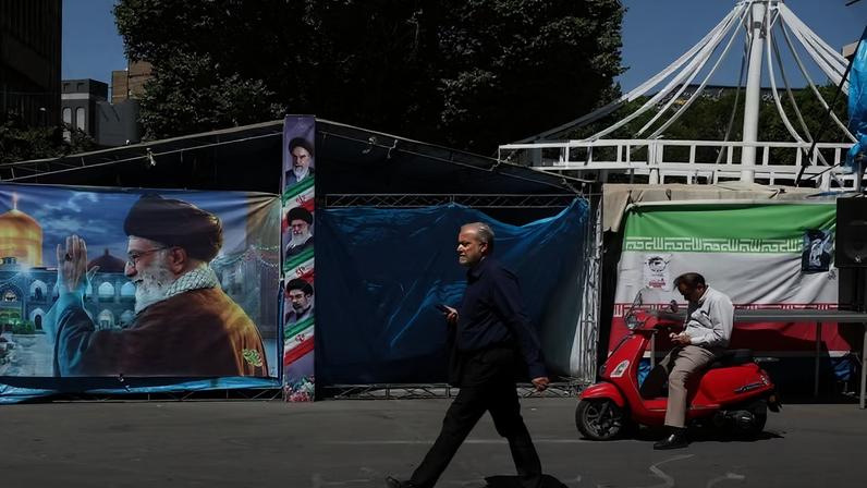 Um homem caminha ao lado de uma faixa com a foto do falecido Líder Supremo do Irã , o Aiatolá Ali Khamenei, em Teerã, Irã , 25 de maio de 2026