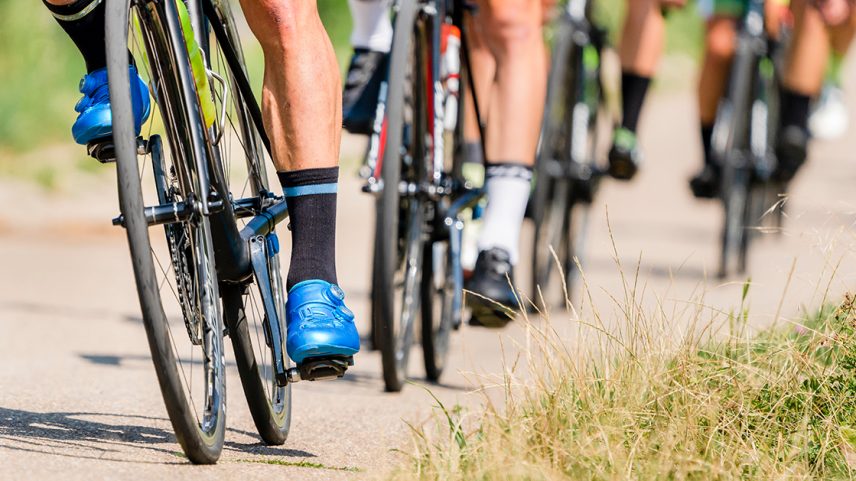 Ciclistas numa fila. Só aparecem pés nos pedais e rodas