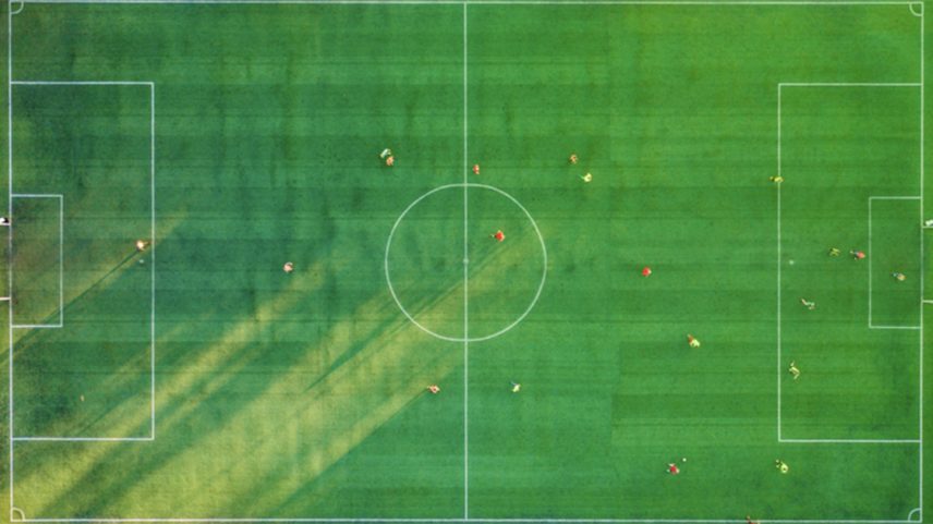 Foto aérea de quadra gramada verde, com jogadores em campo