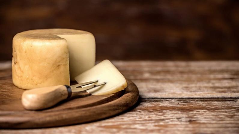 queijo redondo, partido, como fatia e garfo sobre uma tábua de madeira