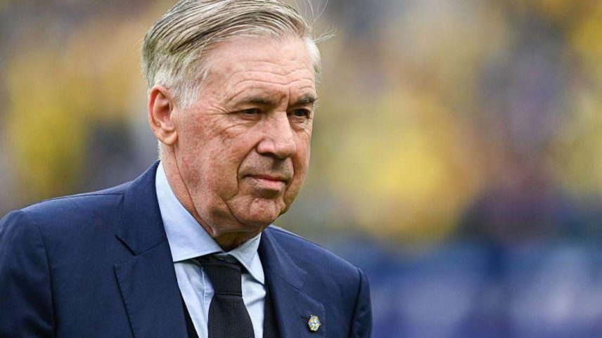 Carlo Ancelotti usando terno e gravata e olhando para um ponto fixo