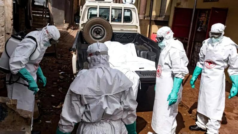 Funcionários da Sociedade da Cruz Vermelha de Uganda são borrifados com desinfetante durante a remoção do corpo de uma suposta vítima de ebola em Kampala, em 26 de maio de 2026.