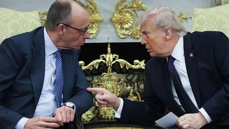 Trump e Merz conversam no Salão Oval. Eles estão sentados e inclinados um em direção ao outro. Trump aponta o dedo para Merz.