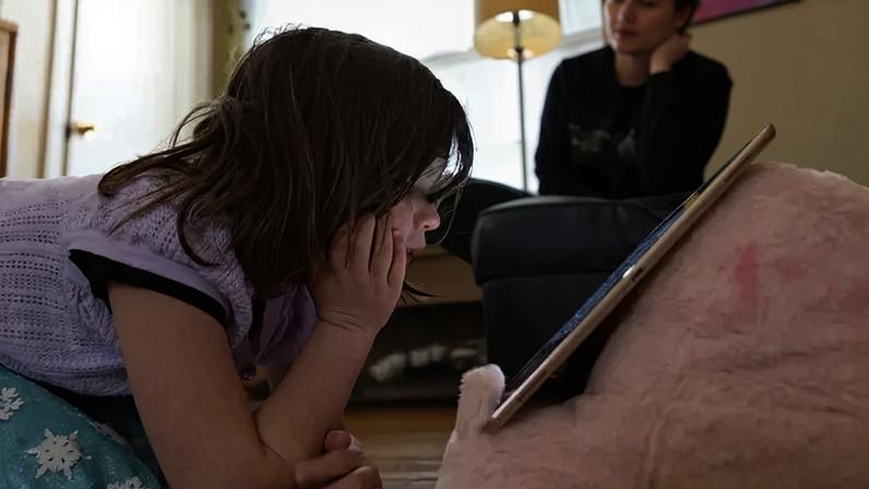 A child leans on her hand as she watches the screen of an Ipad.