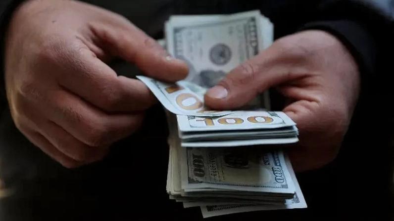 Homem conta notas de US$100 20 de dezembro de 2025 Majid Asgaripour/WANA (Agência de Notícias da Ásia Ocidental) via REUTERS