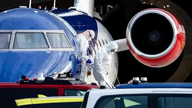 People wearing personal protective clothing disembark a plane.