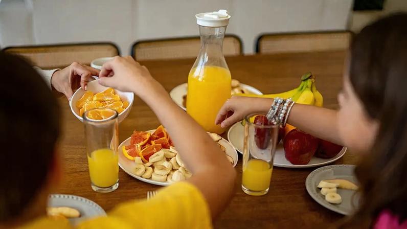 Fotografia de uma mesa de frutas com crianças comendo.