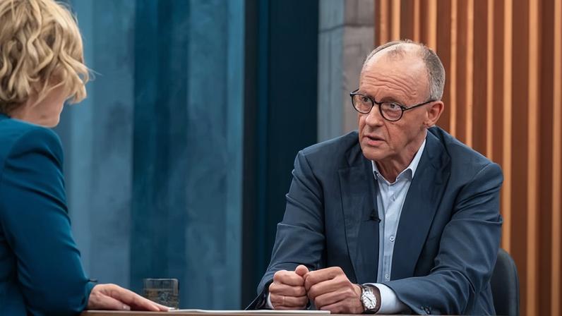Friedrich Merz speaking to Caren Miosga across a TV studio interview table