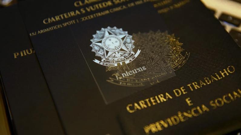 Carteira de trabalho digital mostrada em celular ao lado de versão física de papel