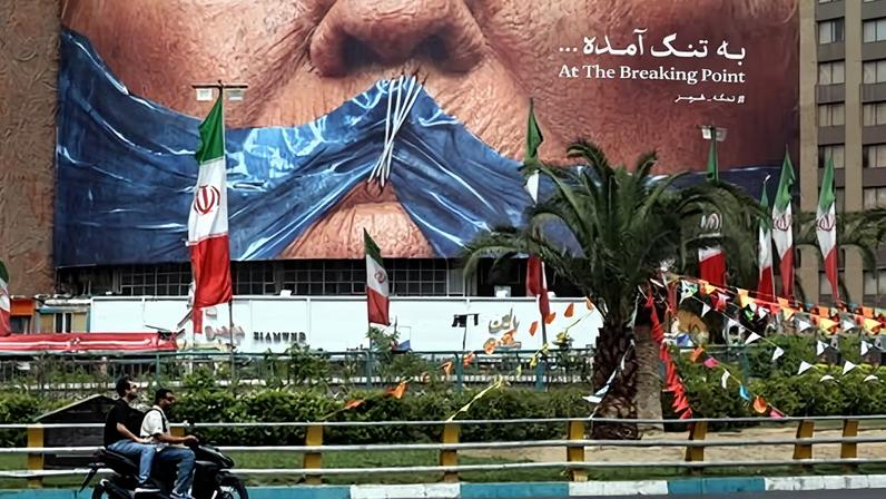Iranians drive past a billboard featuring US President Donald Trump and the strait of Hormuz, erected on Valiasr Square in Tehran 28 May 2026.