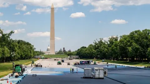 Reuters Workers and work trucks in the drained Lincoln Memorial reflecting pool, which is partially painted blue, with the Washington Monument in the background