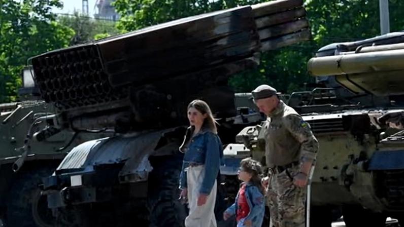 A wounded Ukrainian serviceman and his family walk next to military vehicles on display in Kyiv on Saturday.