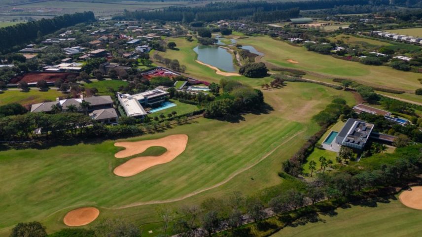 Vista aérea de campo de golfe com lago e casas do Fazenda Boa Vista: destino dos muito ricos