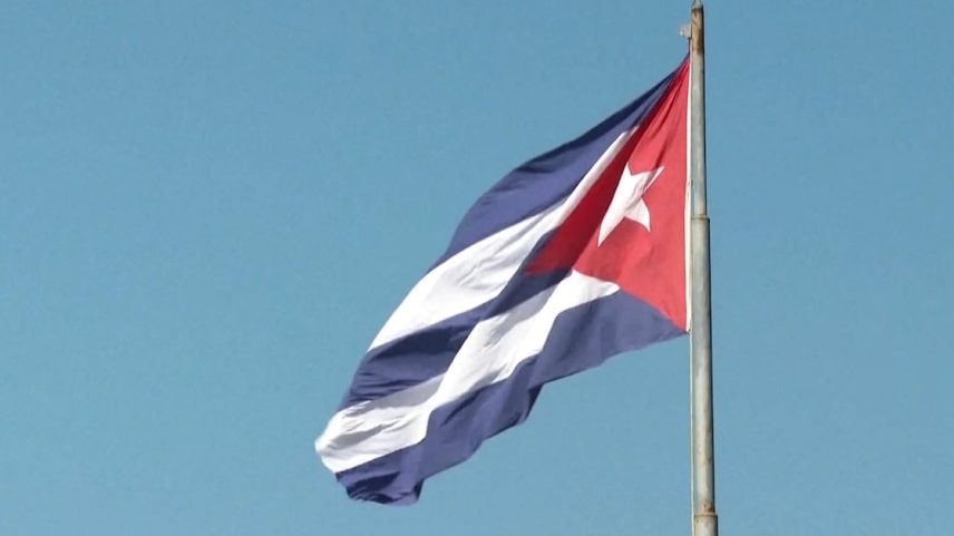Bandeira de Cuba (com listras azuis e brancas e uma estrela branca em meio a um triângulo na horizontal) tremulante em um céu azul
