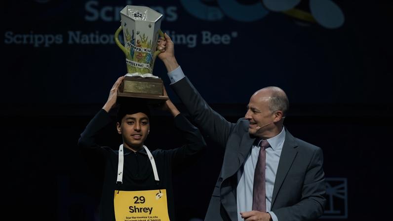 EW Scripps Company president and CEO Adam Symson, right, gives the trophy to Shrey Parikh, winner of the 2026 National Spelling Bee.